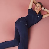 Woman in navy blue scrubs lounging with pink background.