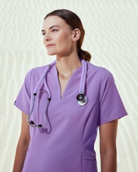 healthcare worker wearing lilac scrubs and stethoscope with sand backgroun