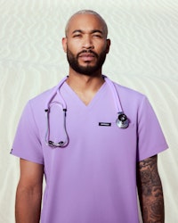 healthcare worker wearing lilac scrubs and stethoscope with sand backgroun