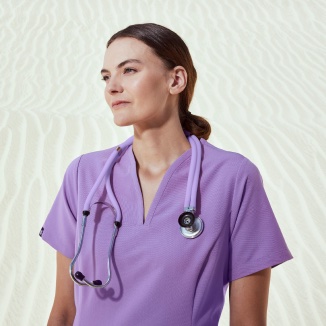 healthcare worker wearing lilac scrubs and stethoscope with sand backgroun