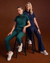 Two women wearing scrubs sitting on stools