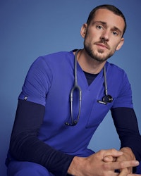 healthcare worker sitting down wearing galaxy blue scrubs and underscrub